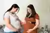 Två gravida personer som känner på varandras magar. Fotografi. 