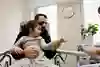 Ett barn sitter i förälderns knä och sträcker fram ett finger till sjuksköterskan.