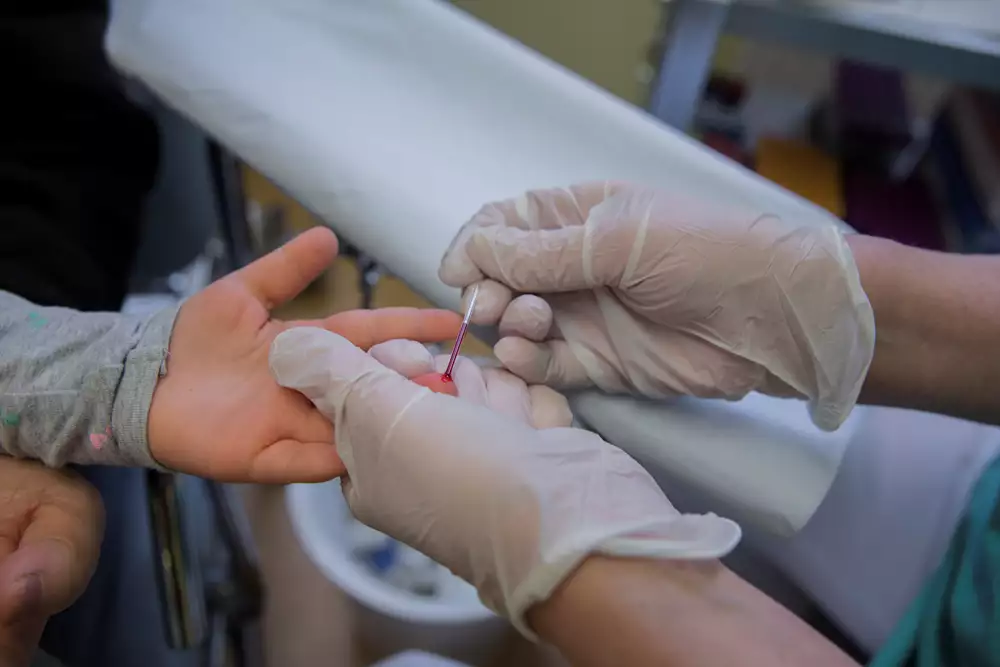 Sjuksköterskan håller ett litet rör mot fingret och samlar upp en bloddroppe.