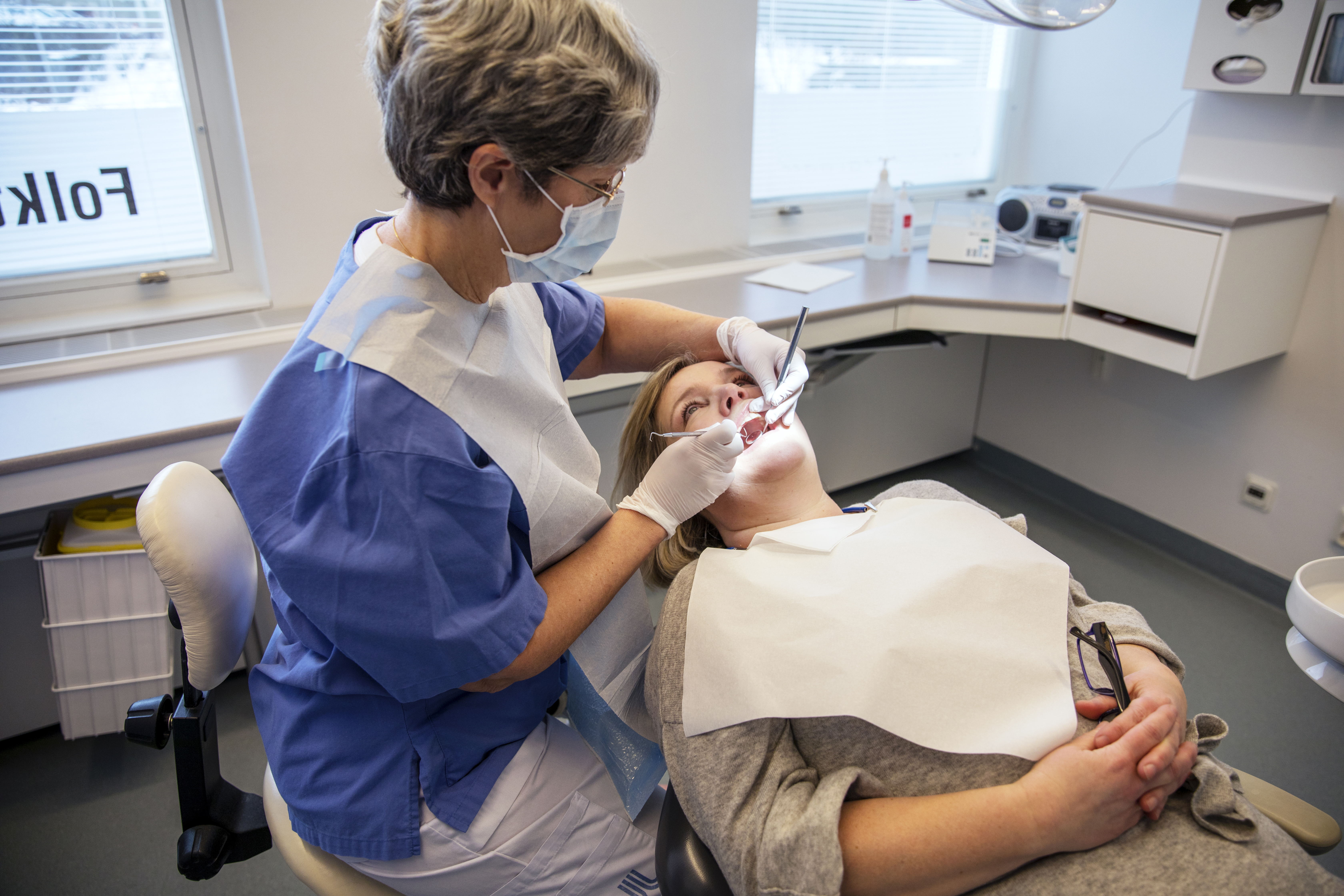 En tandhygienist undersöker på tänderna på en patient i en tandläkarstol.