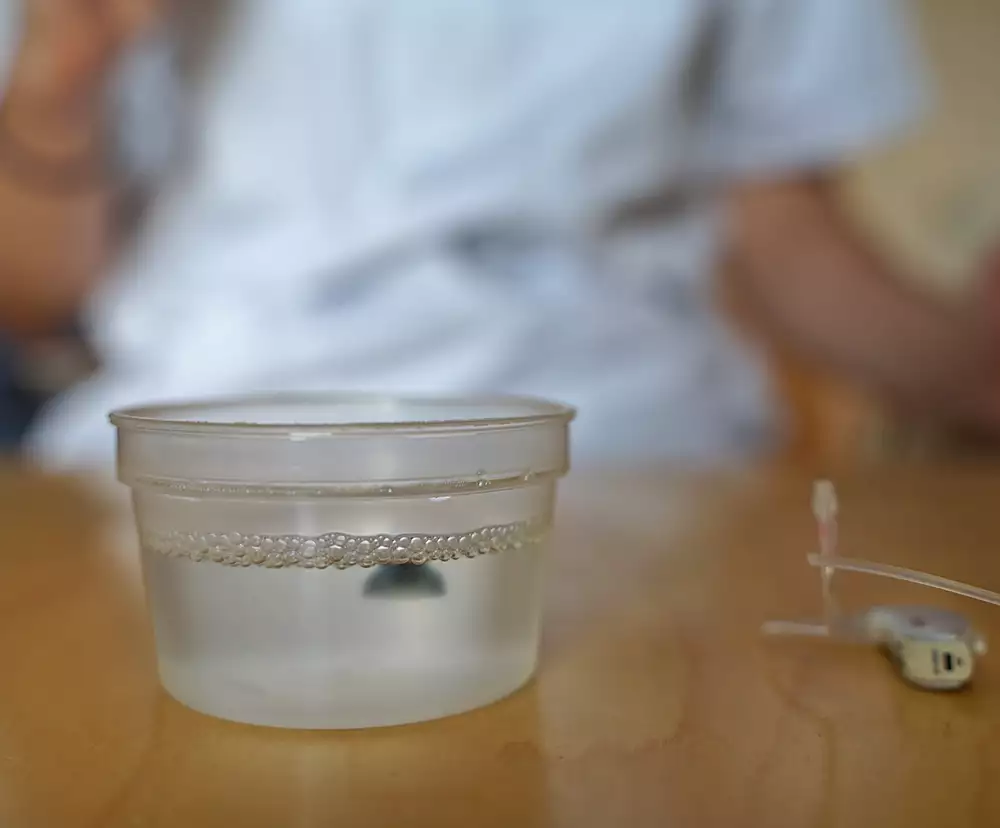 En dome från en hörapparat ligger i ett glas med vatten och diskmedel.