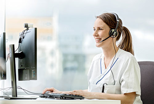 Tandläkare sitter framför dator och pratar med en patient via ett headset.