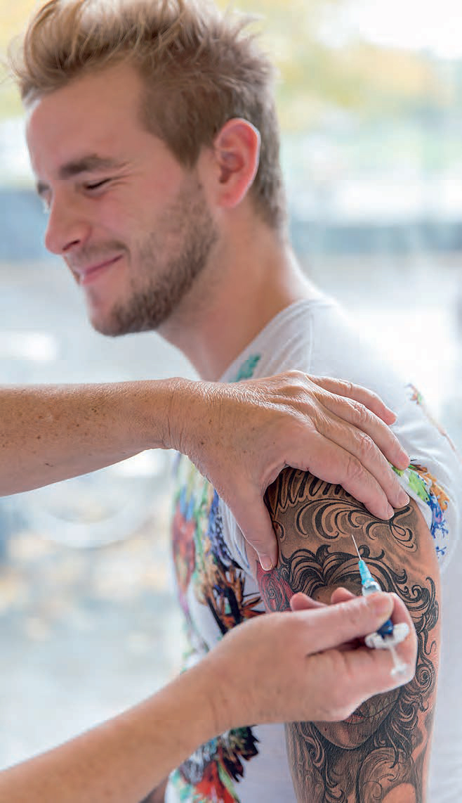 En tatuerad person får en spruta i överarmen. 