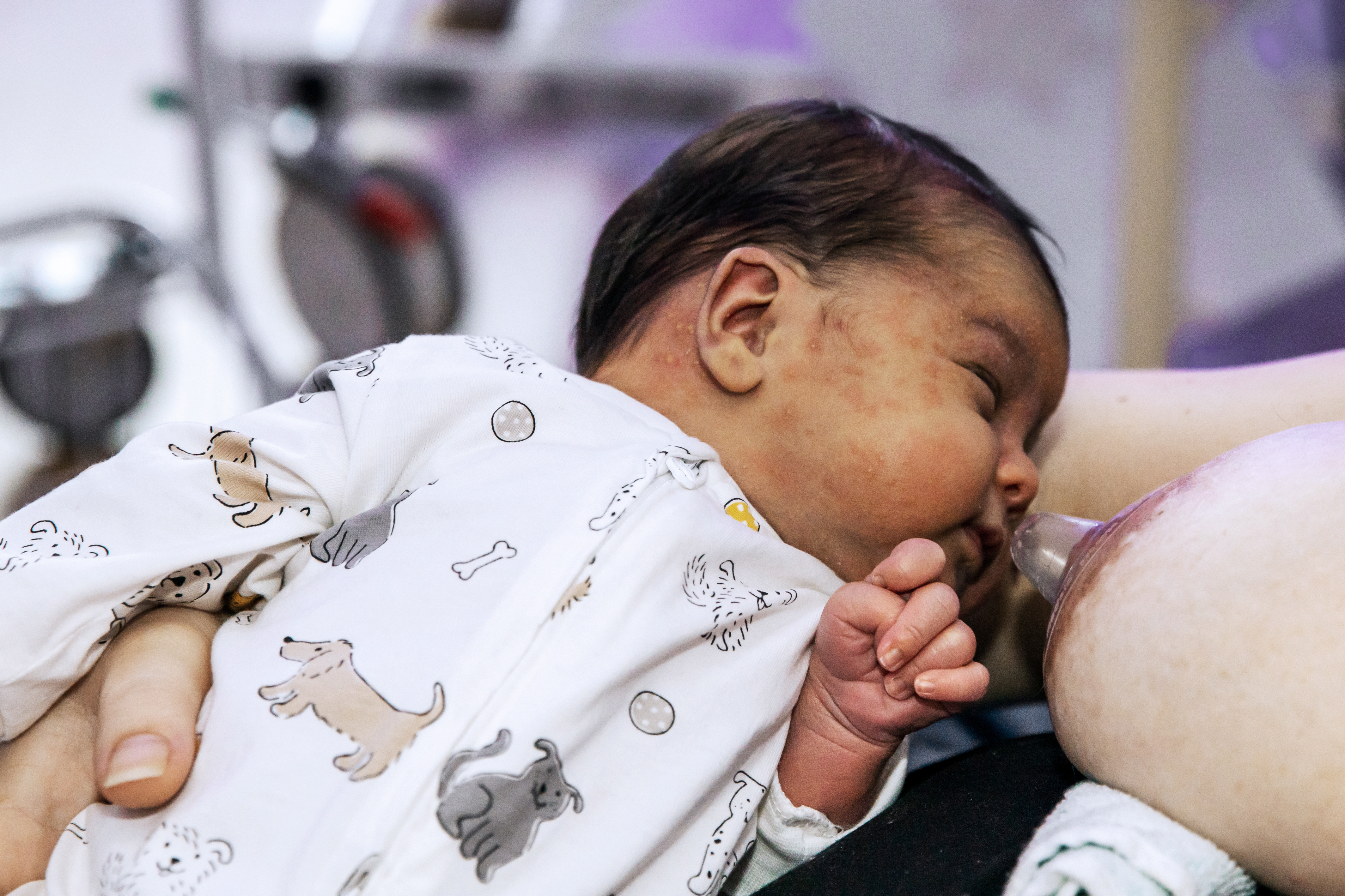 Bebis som ligger bredvid ett bröst med amningsnapp.