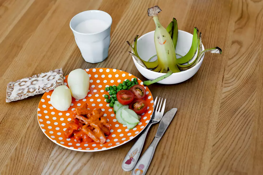En tallrik med kött, potatis och grönsaker, och ett glas mjölk, ett knäckebröd med smör och en halv banan