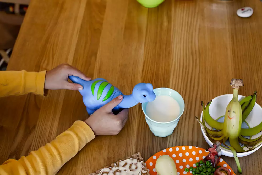 Ett barns händer håller i en leksak vid ett bord med mat.