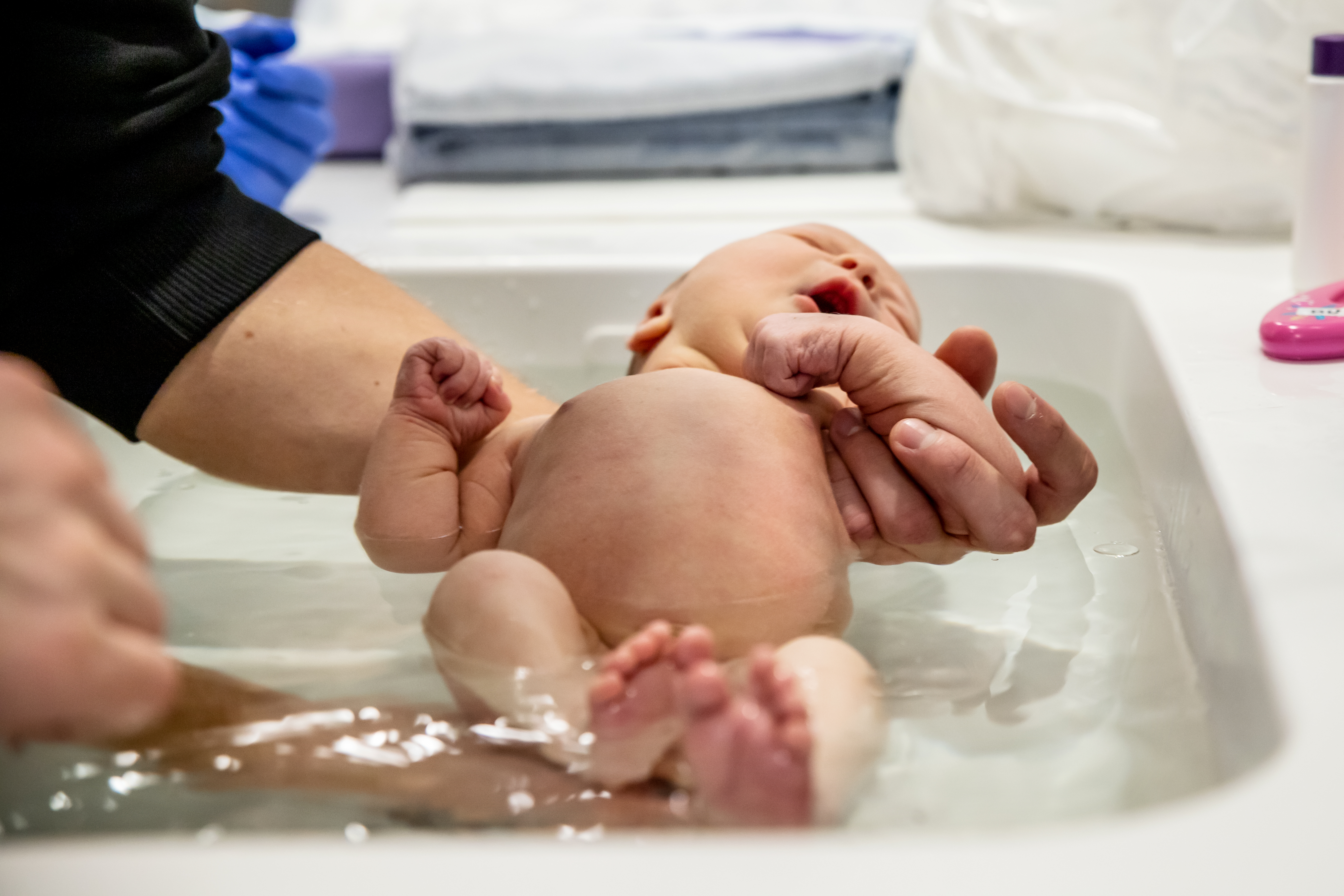 En vuxen person badar ett nyfött barn i en balja.