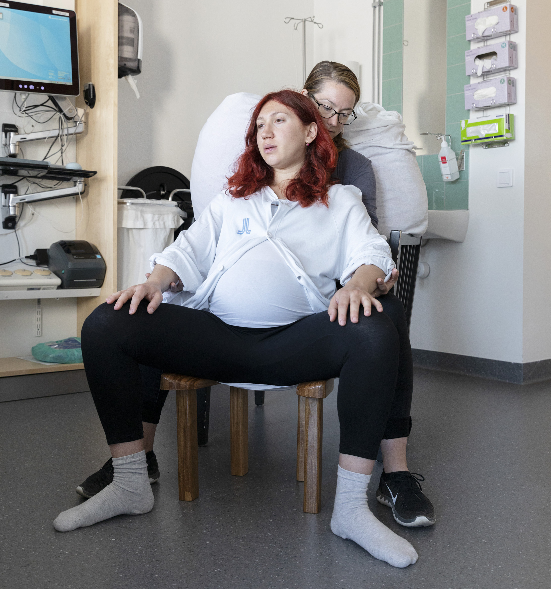 Gravid kvinna i ställning för att föda på pall, med sin partner bakom sig.