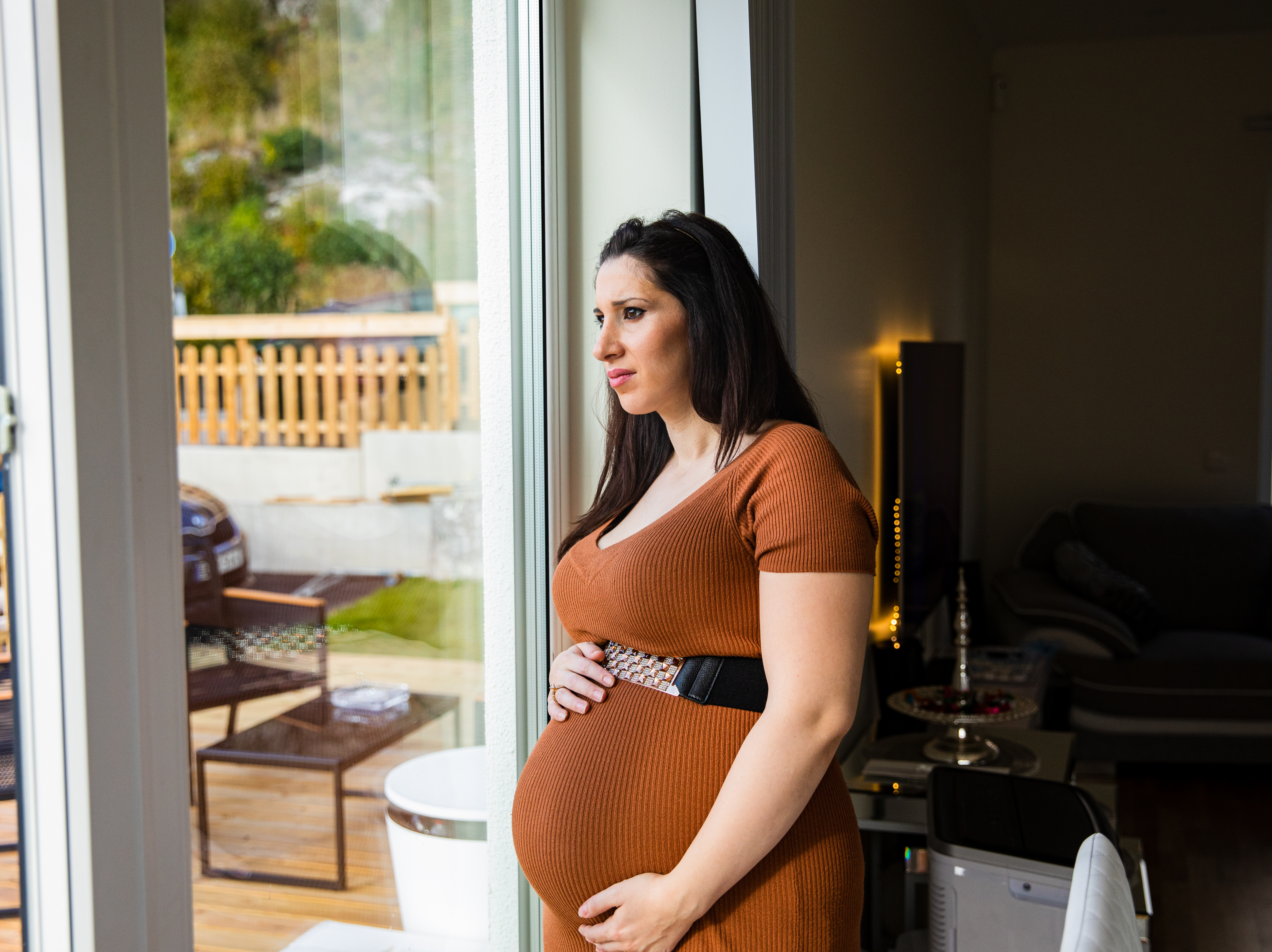 En gravid person tittar ut genom ett fönster och funderar. Fotografi. 
