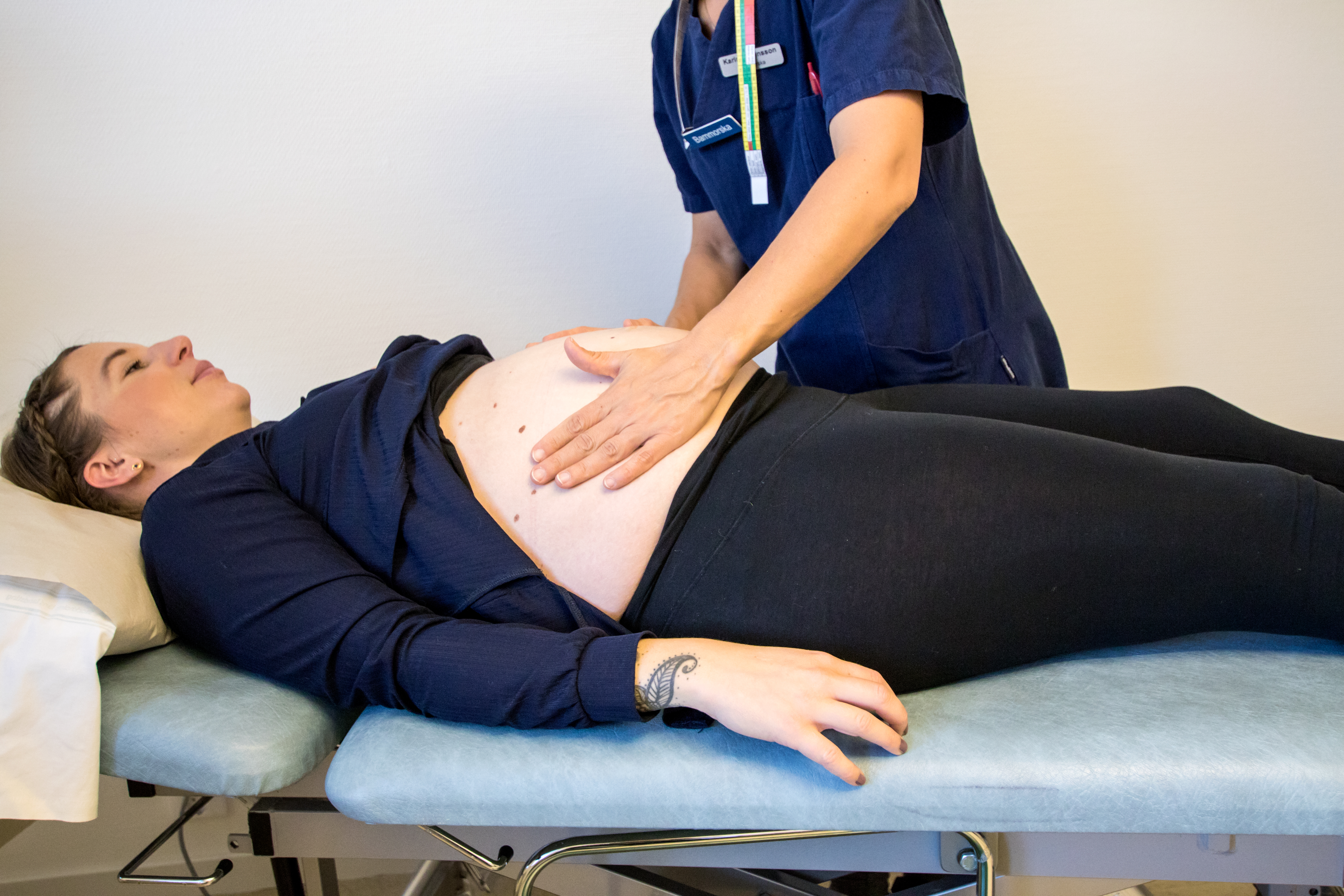 En gravid kvinna ligger på en brits och en barnmorska känner på magen.