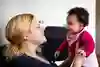 En mamma håller upp sin bebis och pratar och ler. 