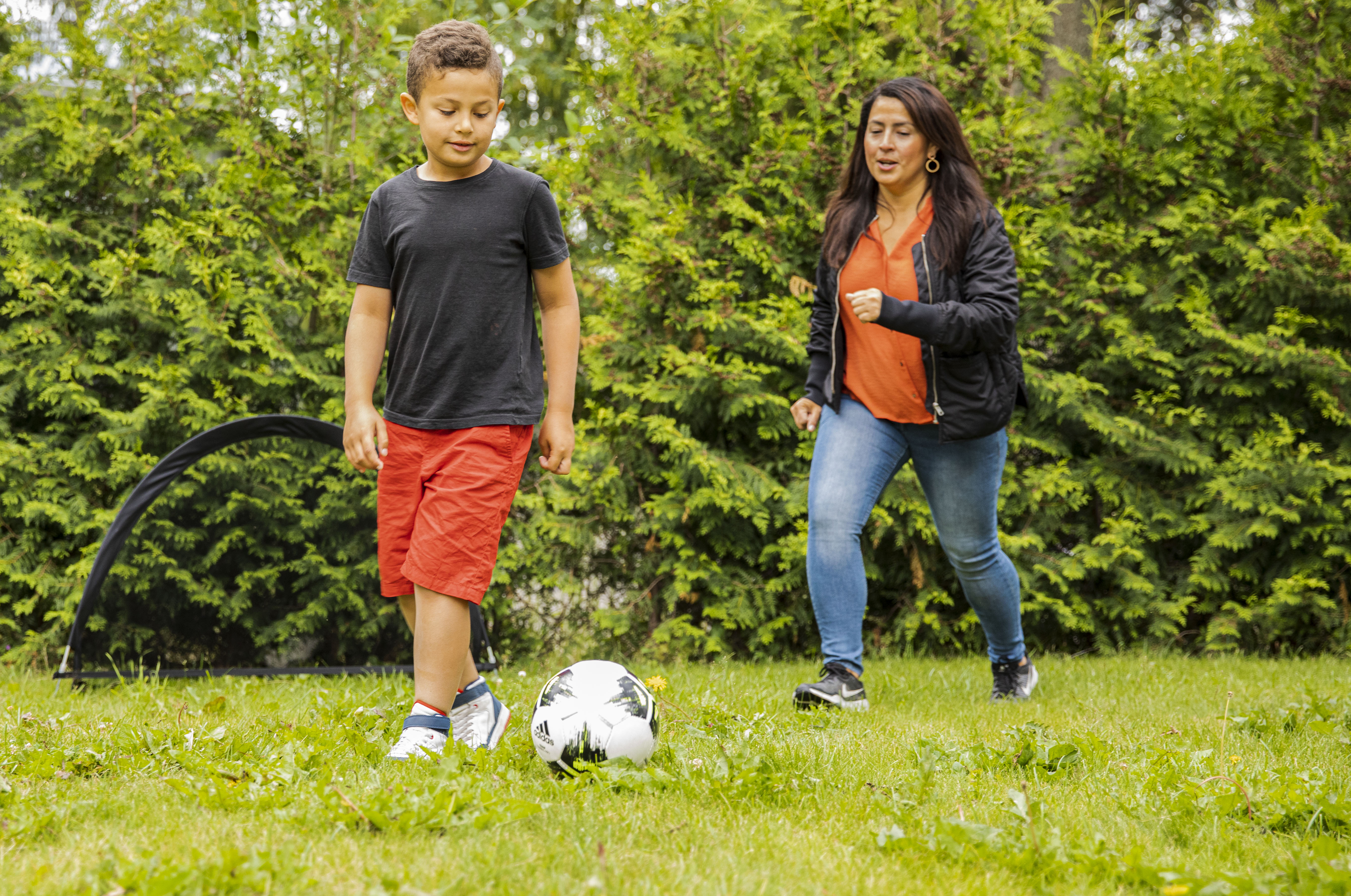 Sjuåring spelar fotboll med en vuxen. Fotografi. 