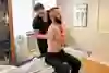En person sitter på en brits och blir behandlad av en kiropraktor. 