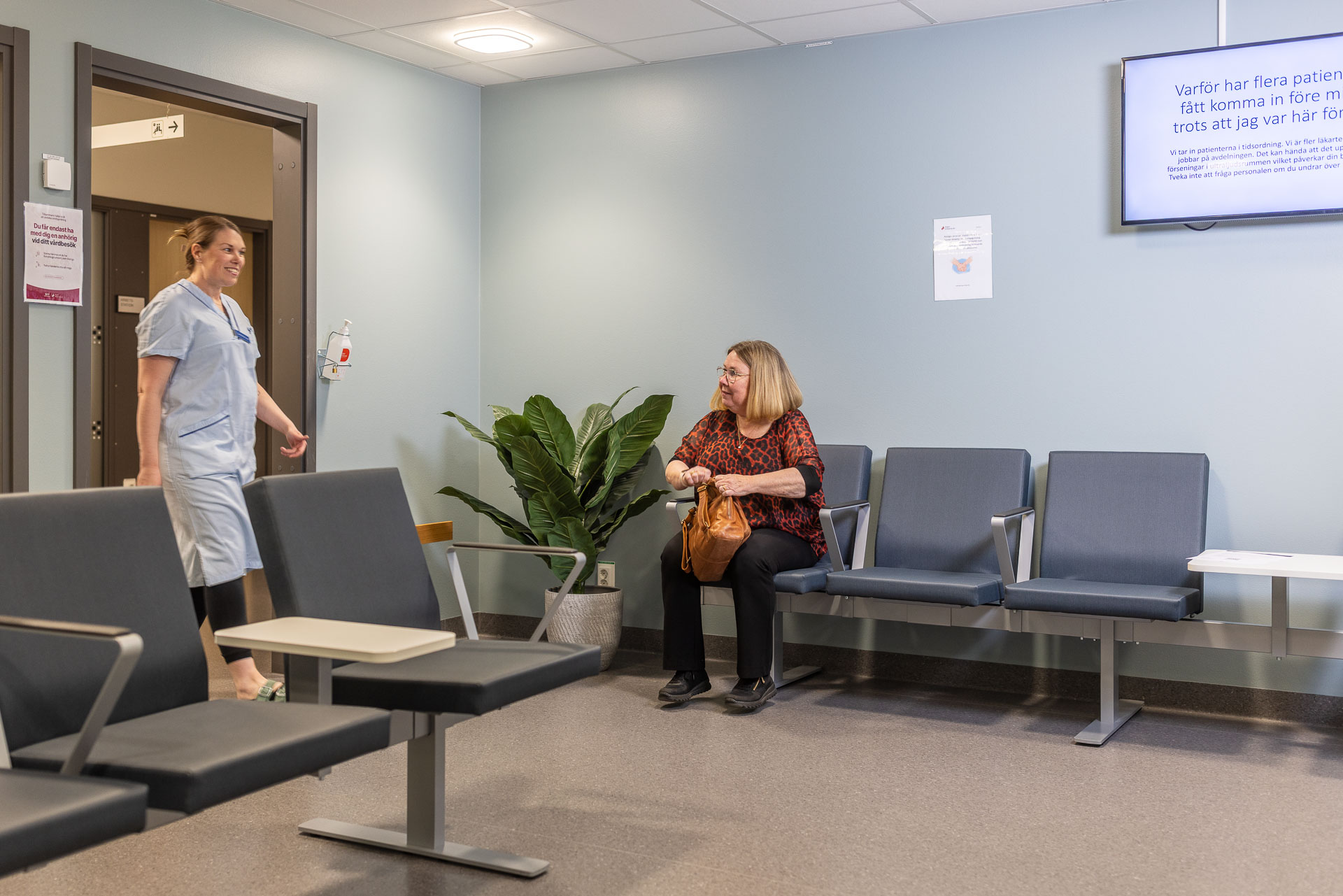 En patient sitter och väntar i ett väntrum medan en vårdperson kommer in genom dörröppningen.