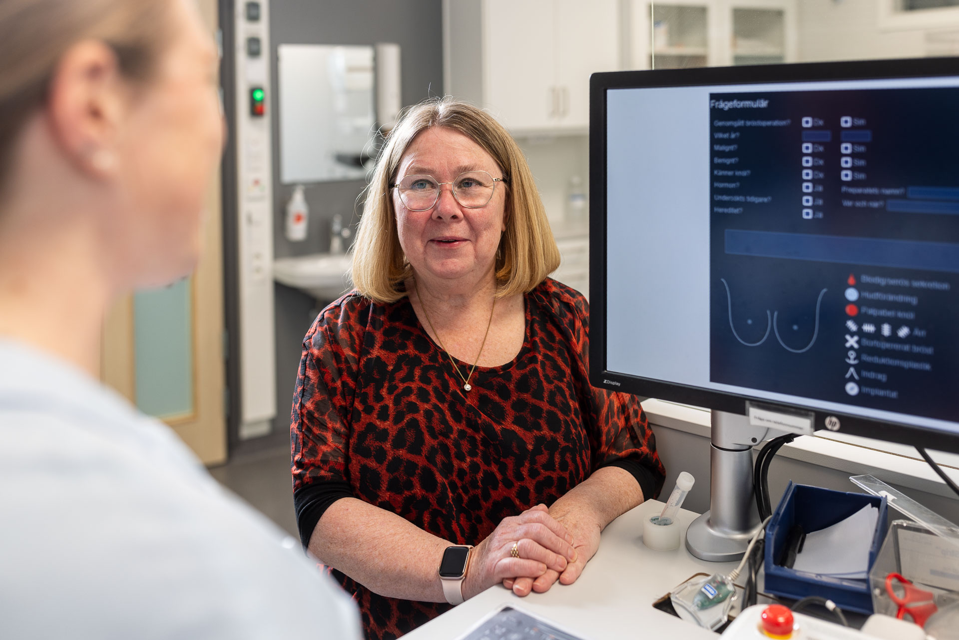 En patient och en vårdperson samtalar framför en bildskärm som visar ett bröst.