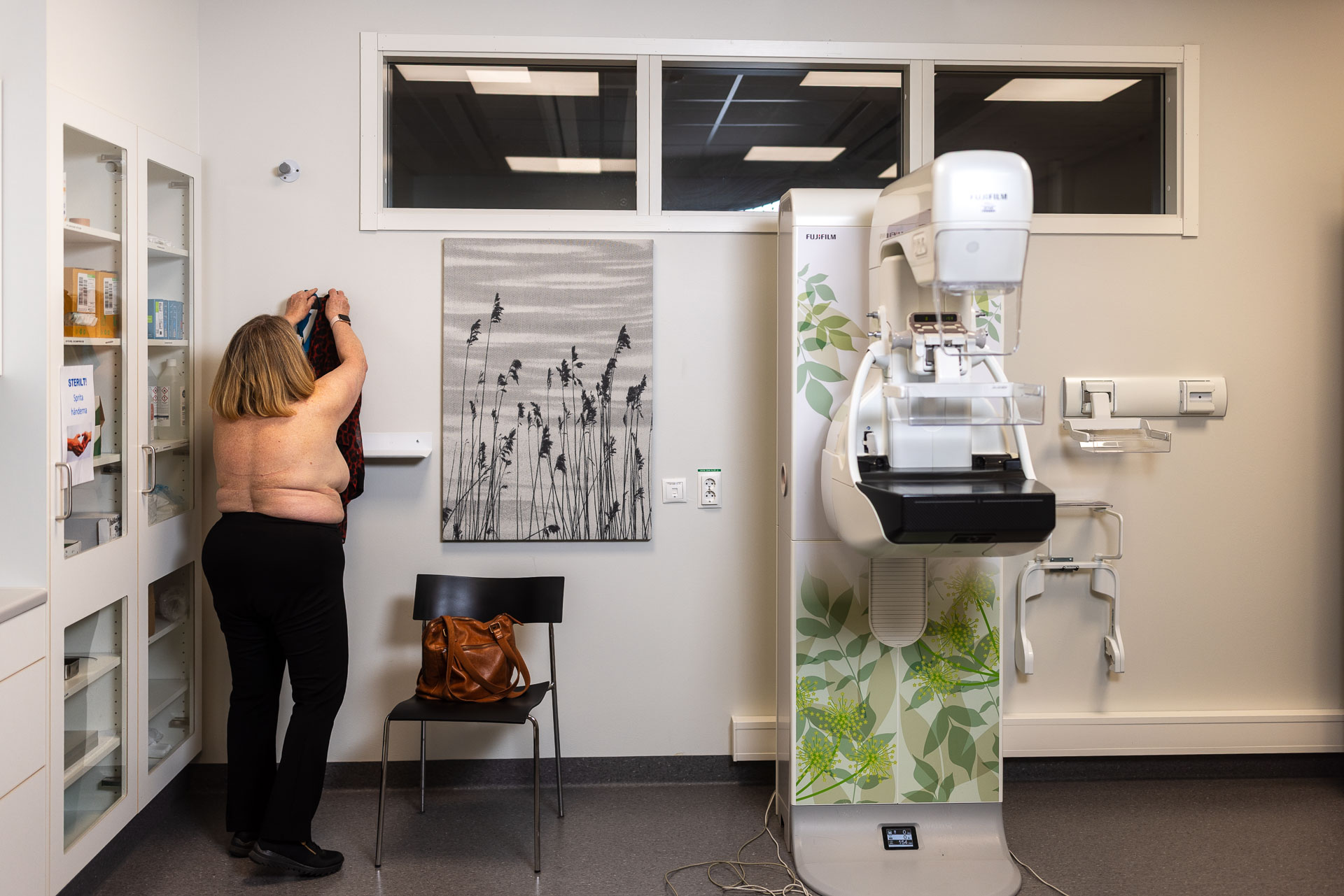 En person med bar överkropp hänger upp en blus i ett undersökningsrum.