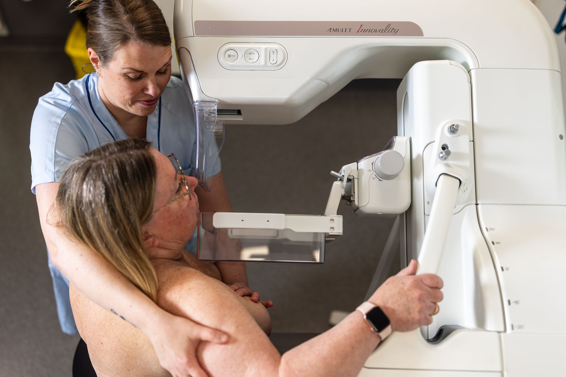 En vårdperson håller runt axlarna på en person och hjälper till att få bröstet på plats i en mammografiapparat.