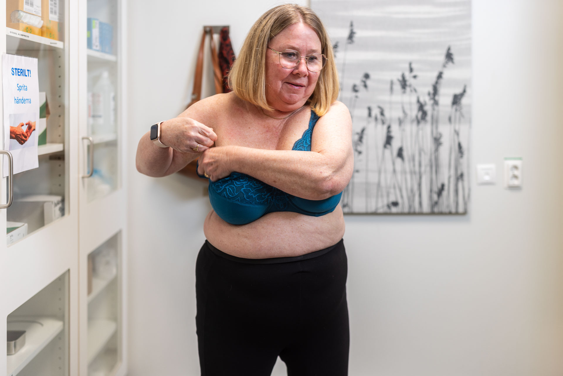 En patient klär på sig sin BH stående i ett vårdrum.