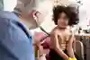 En läkare lyssnar på lungorna på ett barn med ett stetoskop. Fotografi. 