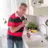 Person som sjunger med en diskborste i handen, vid diskbänken i ett kök.