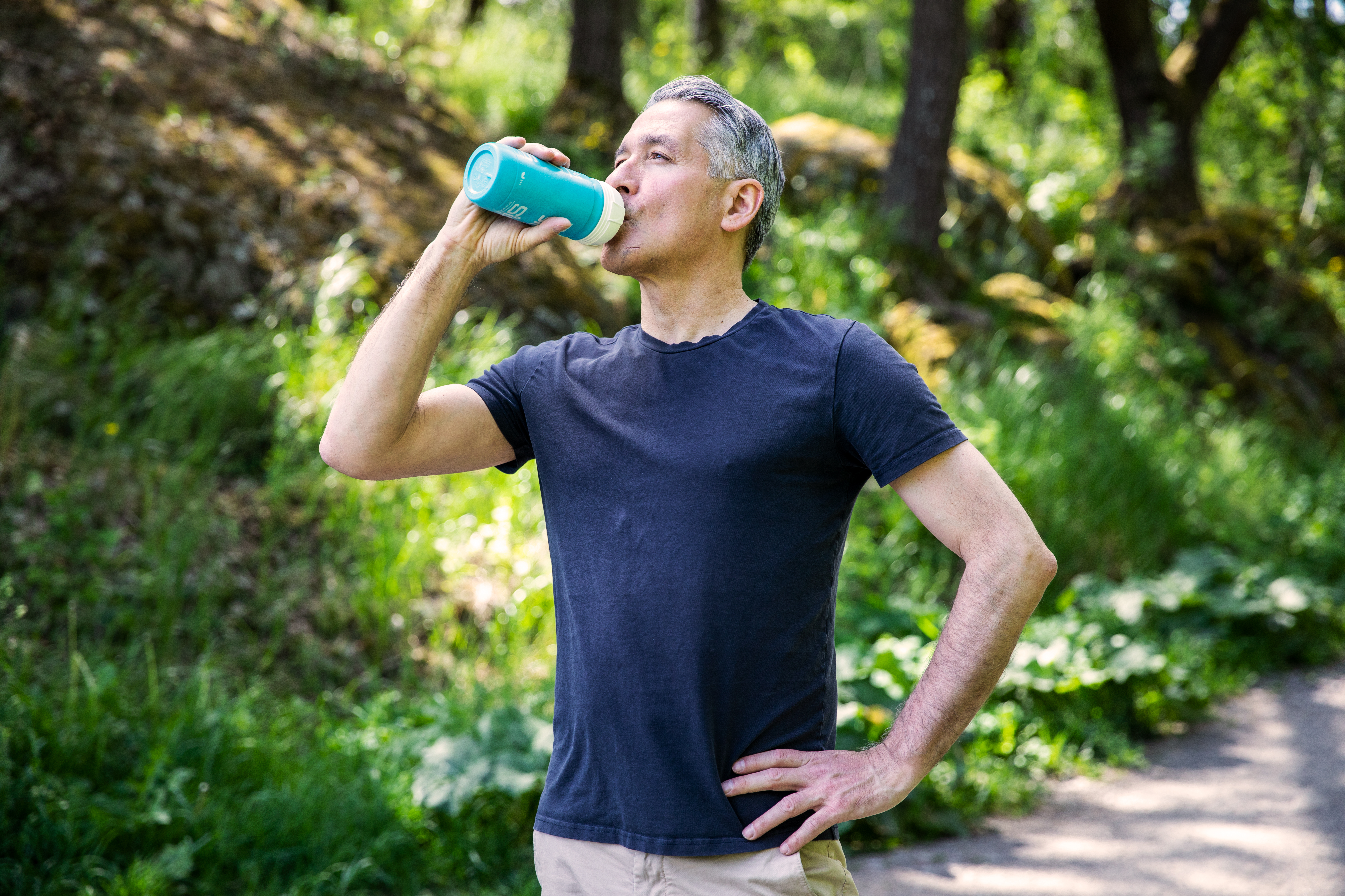 Man som dricker vatten ur en vattenflaska utomhus på sommaren.