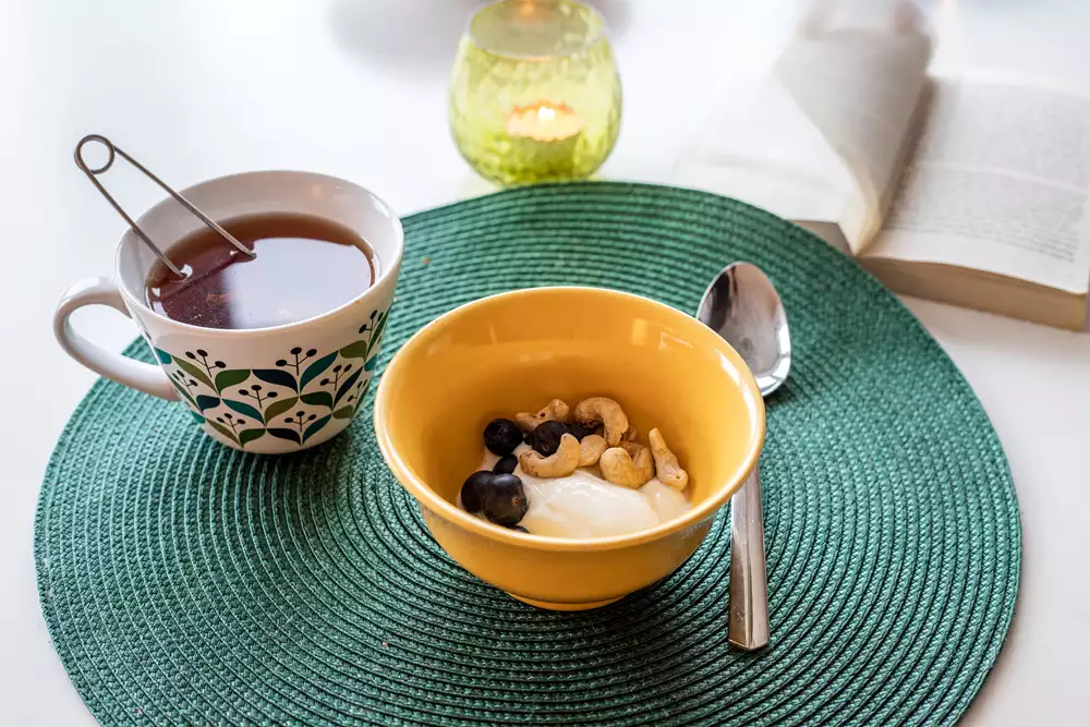 Yoghurt med blåbär, cashewnötter och en kopp te. Fotografi.