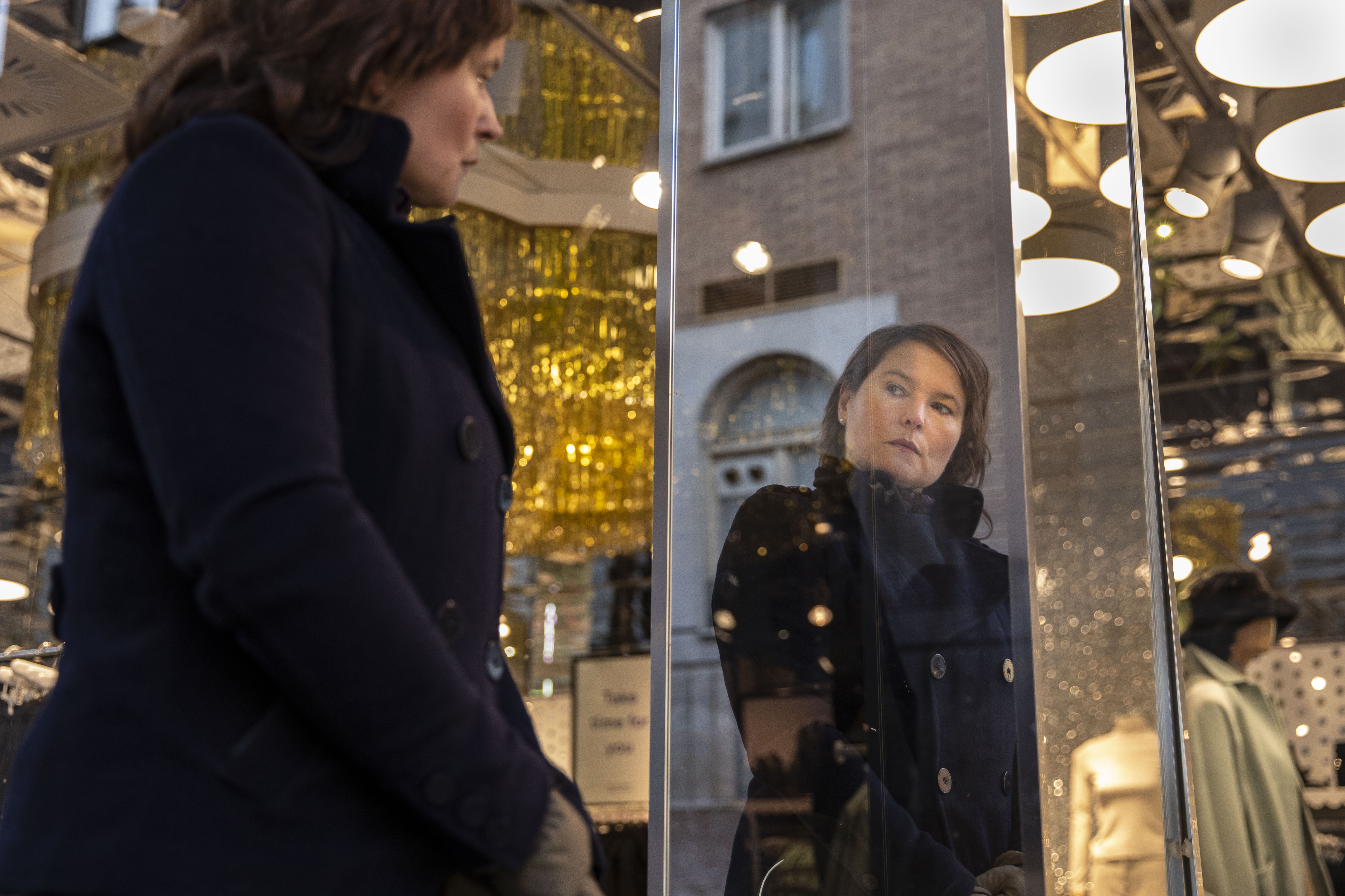 Person som ser sin spegelbild i ett skyltfönster, omgiven av skyltdockor.