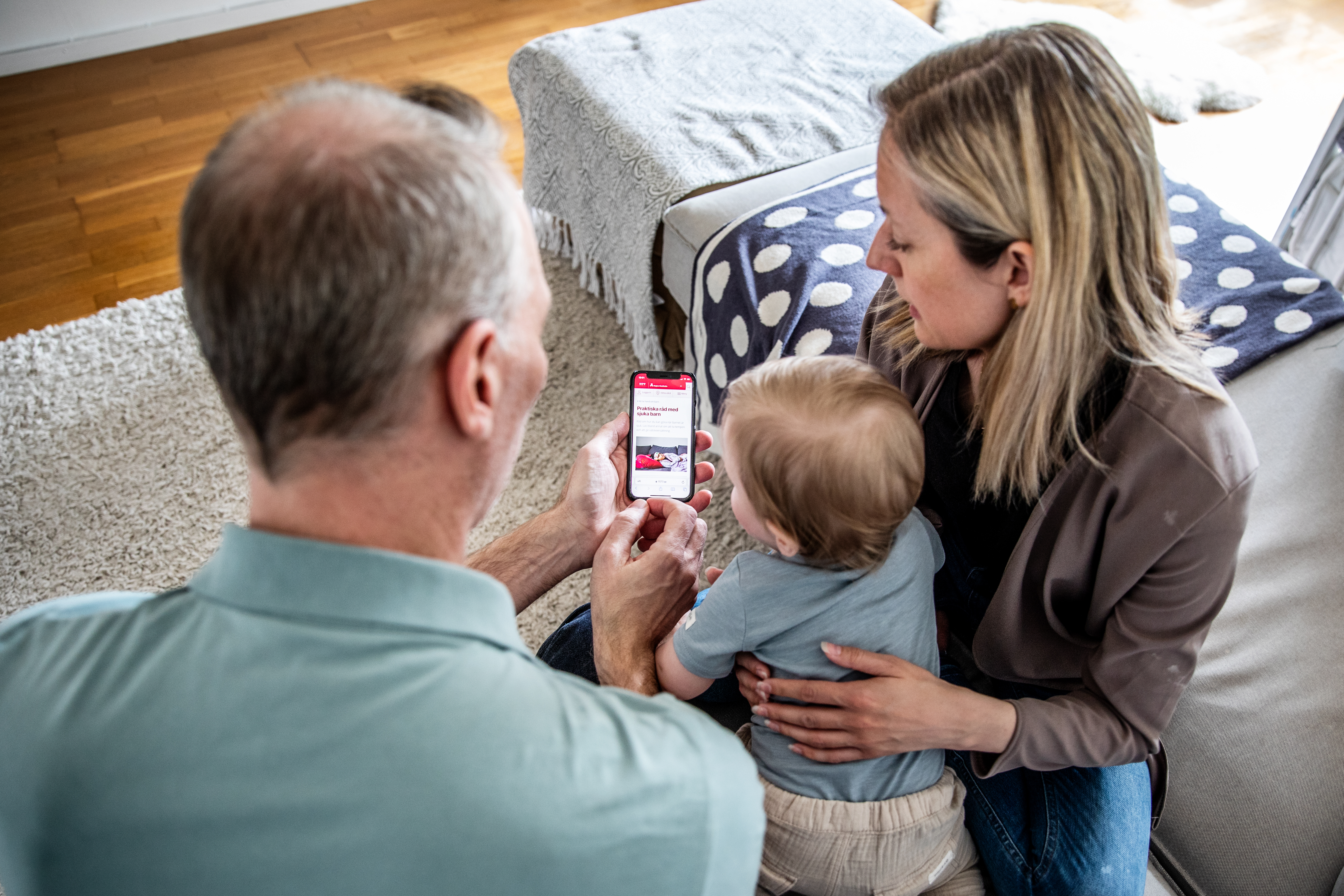 Två vuxna och ett barn tittar på en mobiltelefon