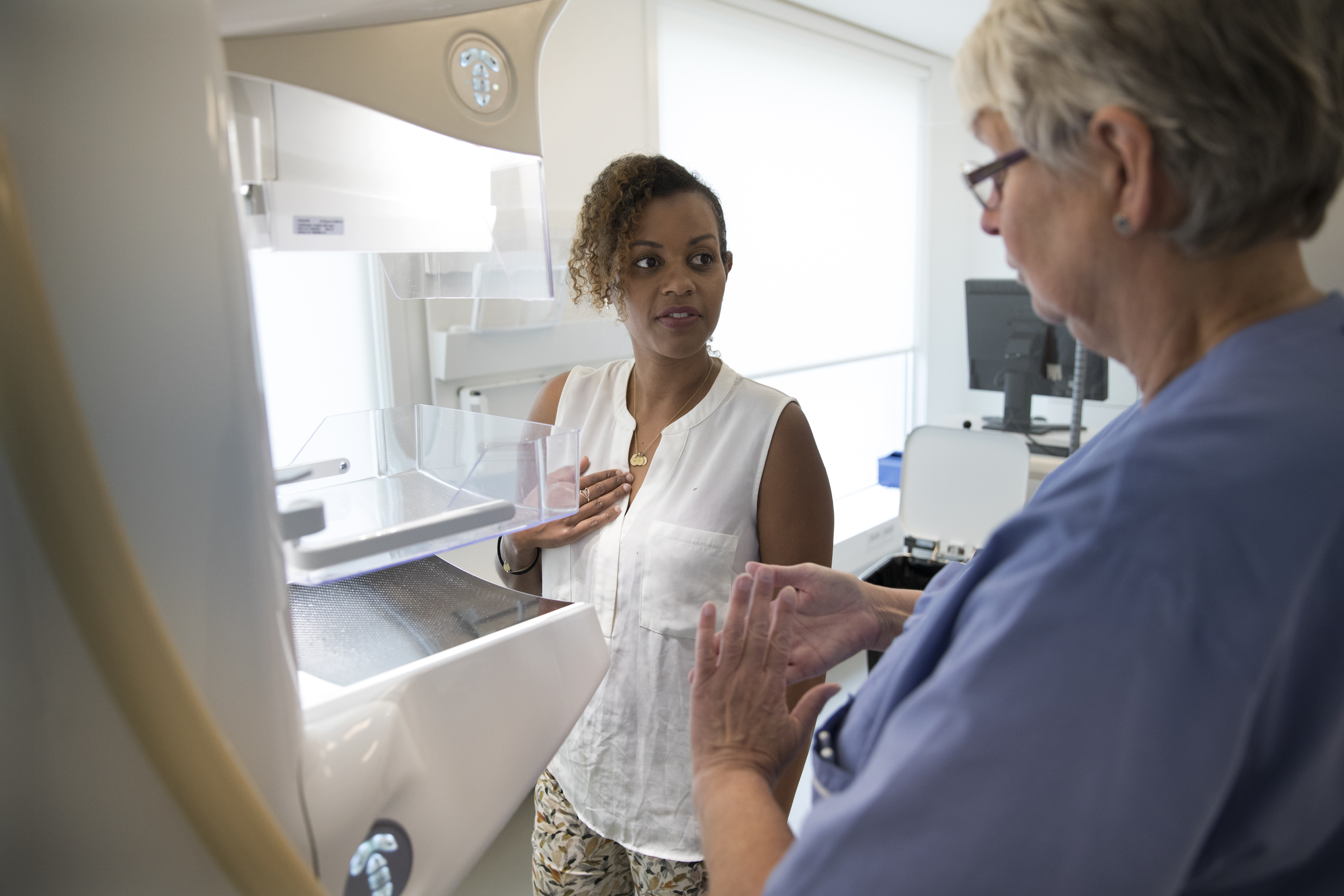 Bild som visar mammografiapparat, en sjuksköterska och en kvinna som ska undersökas