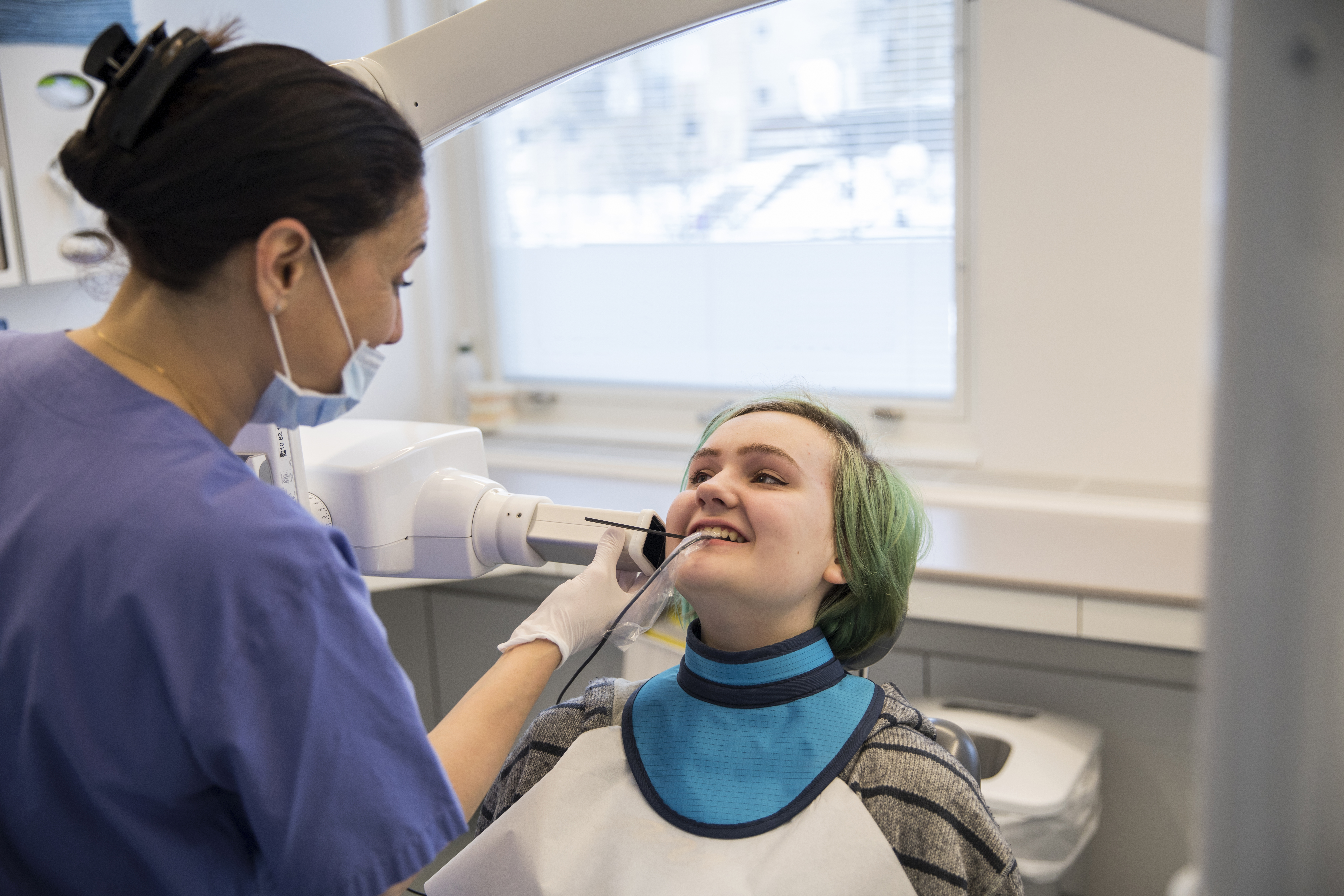 Person som sitter i en tandläkarstol och ska röntga tänderna. 