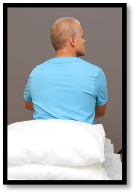 Person sitter på säng med kudde bakom ryggen.