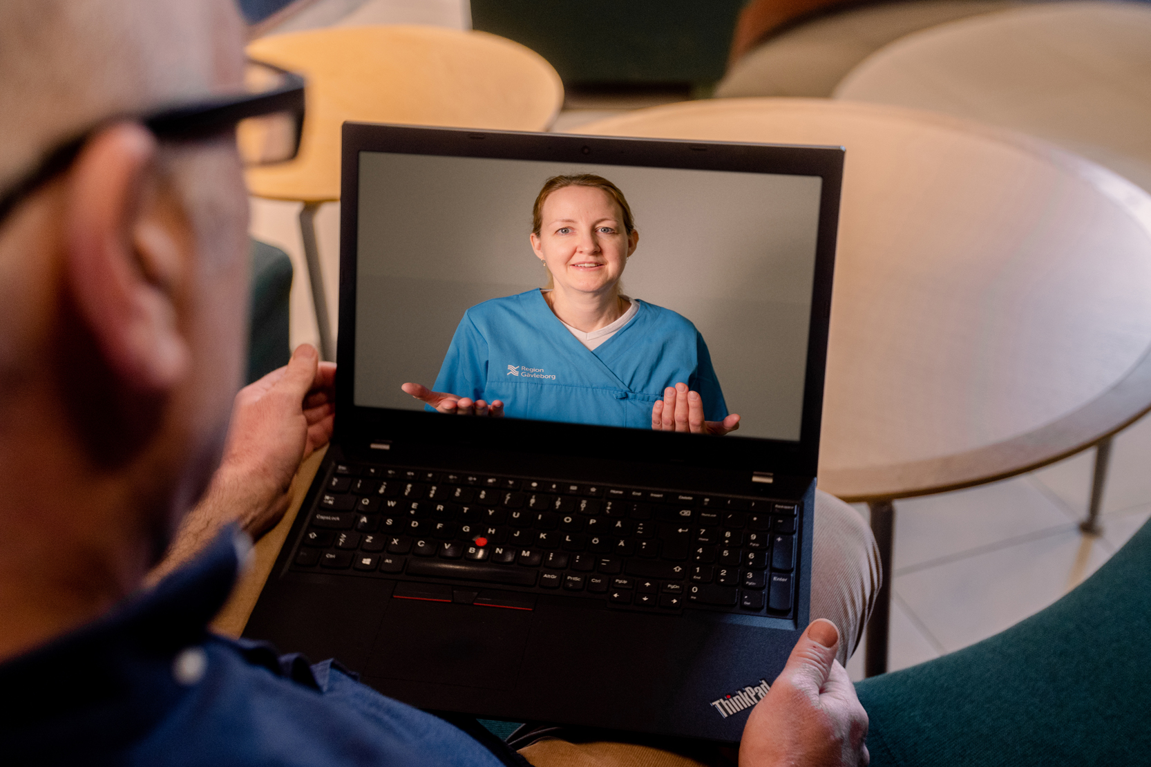 Person sitter med dator i knä och samtalar med vårdpersonal genom datorn