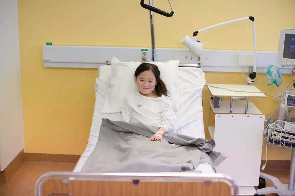 Barn som ligger i en sjukhussäng med plåster på handen.