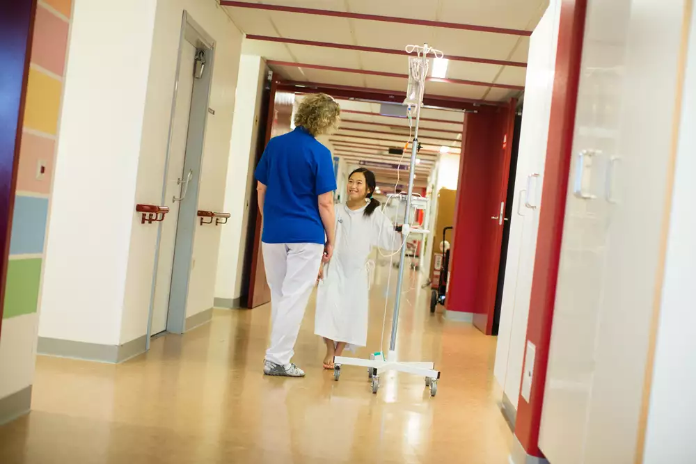 Ett barn med droppställning pratar med vårdpersonal i en sjukhuskorridor.