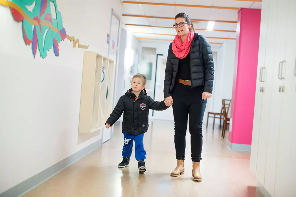 Ett barn och en förälder går hand i hand i en sjukhuskorridor.
