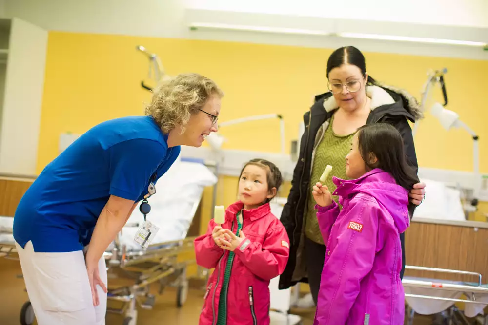 Förälder med två barn som äter glass säger hejdå till vårdpersonal i vårdrum på sjukhus.