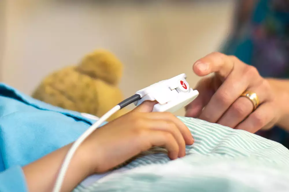Ett barn ligger i en sjukhussäng och har ett mätinstrument på sitt finger.