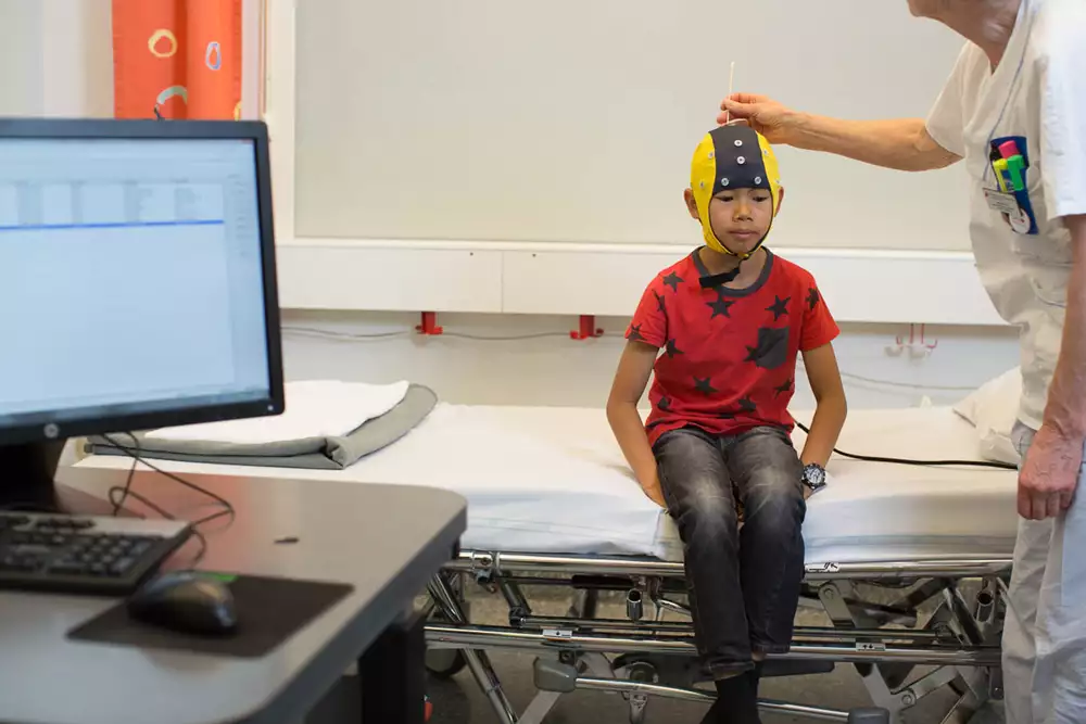 Vårdperson petar med en pinne med gel genom hålen på specialmössa inför sömn-EEG.