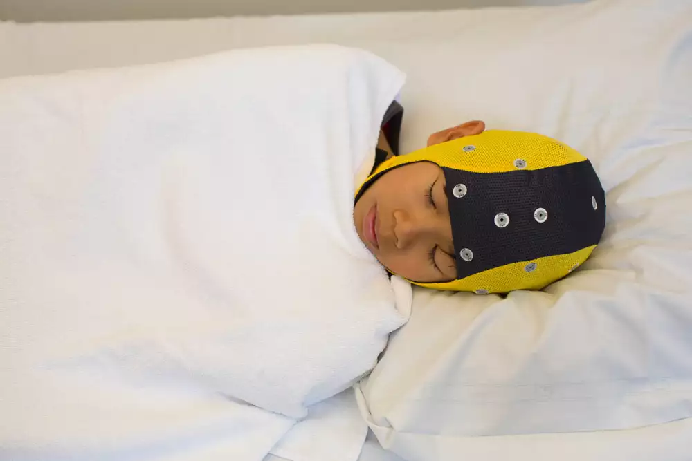 Barn med gul och svart specialmössa ligger och sover under sömn-EEG.