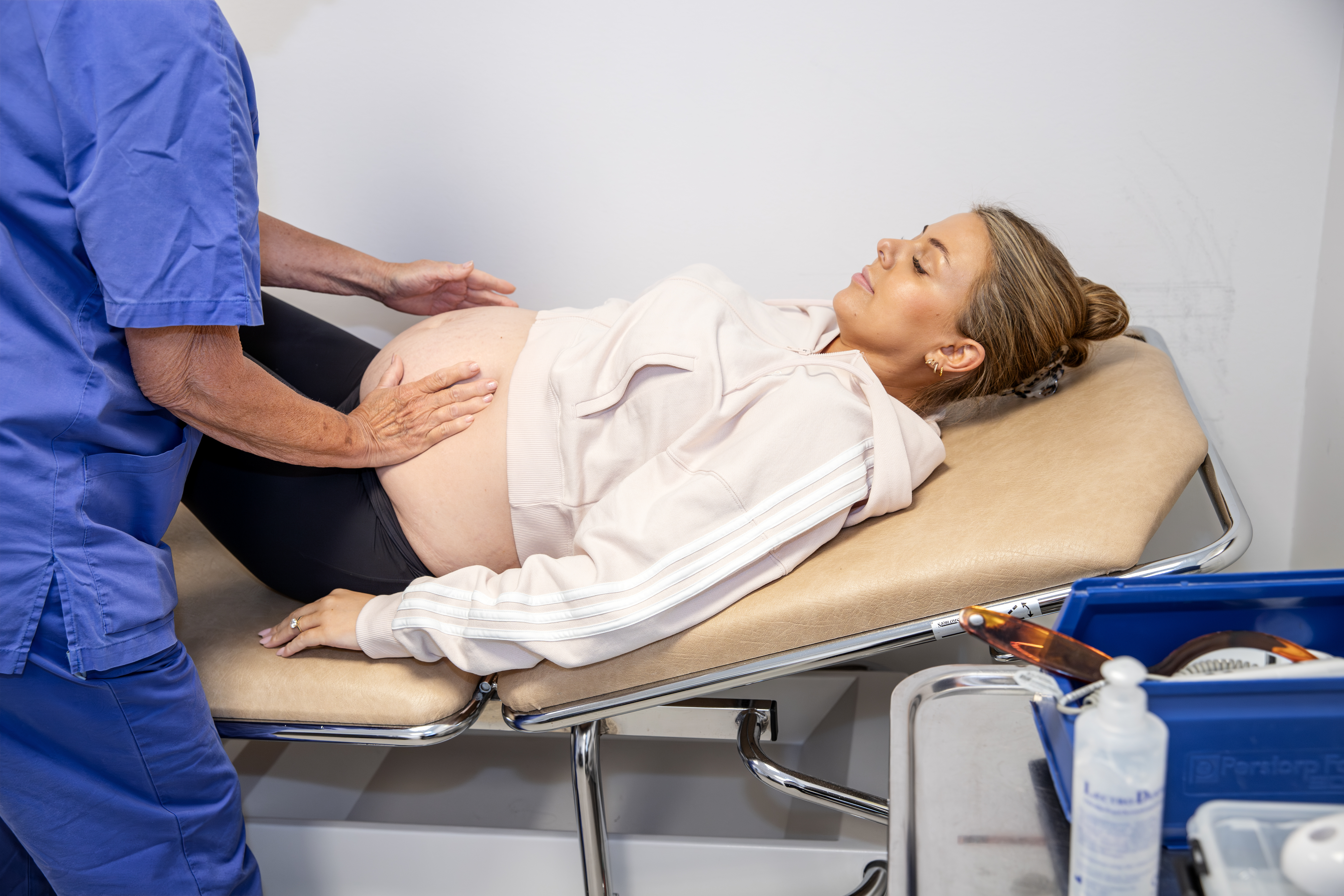 En gravid patient ligger på en brits och en barnmorska känner på patientens mage.
