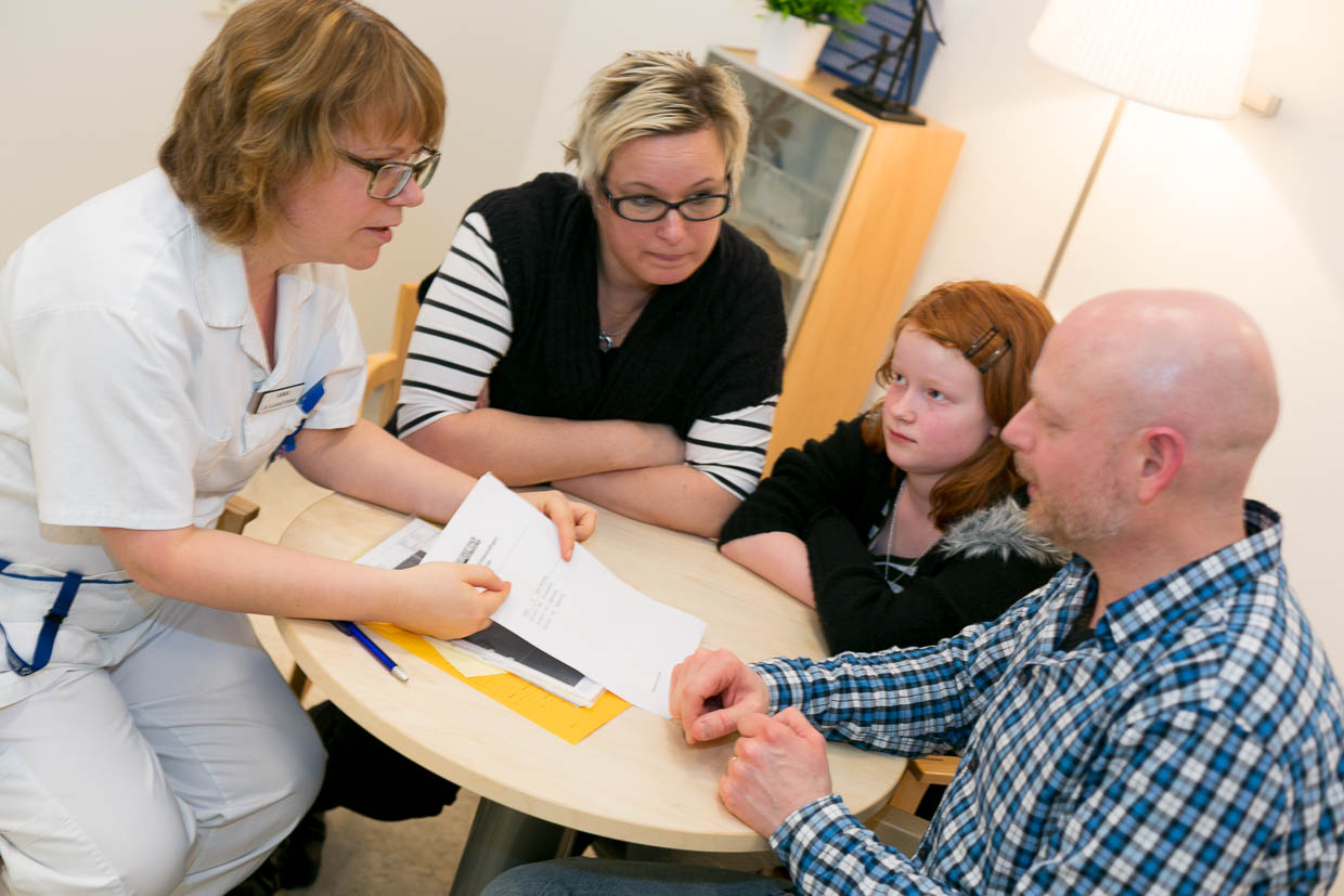 Patient med anhöriga sitter ihop med vårdperson runt ett bord och pratar.