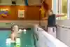Man i pool som får instruktioner om hur han ska träna med flythantlar i vattnet. Instuktören står på land och visar