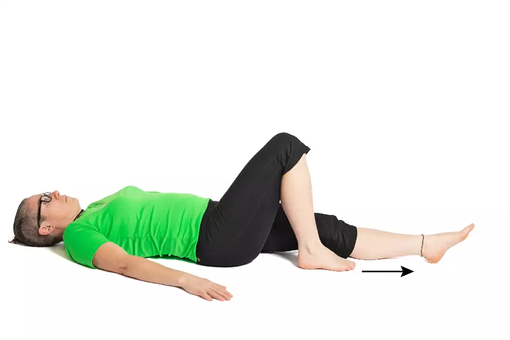 En person ligger på rygg med högra benet böjt och knät uppåt. En pil pekar utmed det vänstra utsträckta benet.