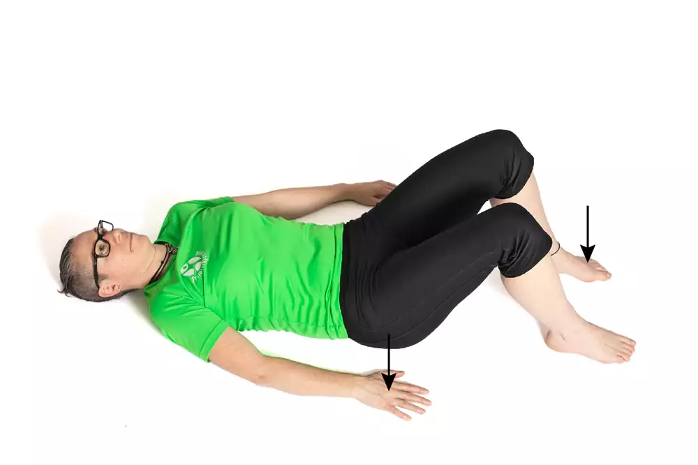 En person ligger på rygg med böjda knän. En pil pekar på höger hand och en annan pil på vänster fot.