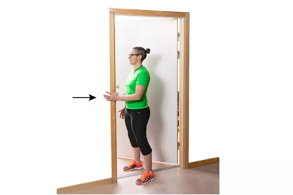 En person står i en dörröppning och håller vänster hand mot dörrposten. En pil pekar mot handen.