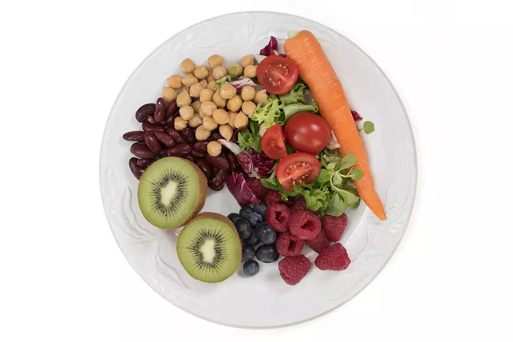 En tallrik med olika frukter och grönsaker, bland annat kiwi, hallon, morot, bönor, tomater och kikärter.