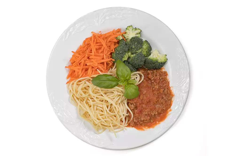 En tallrik med spagetti, köttfärssås, riven morot och broccoli.