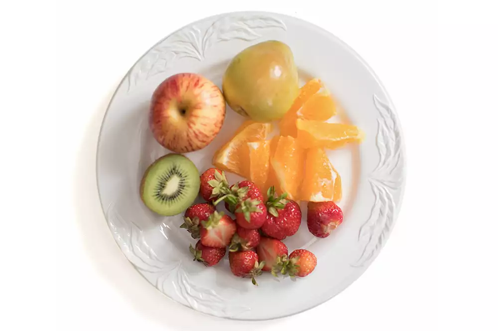 En tallrik med olika frukter, bland annat äpple, kiwi, jordgubbar och apelsinklyftor.
