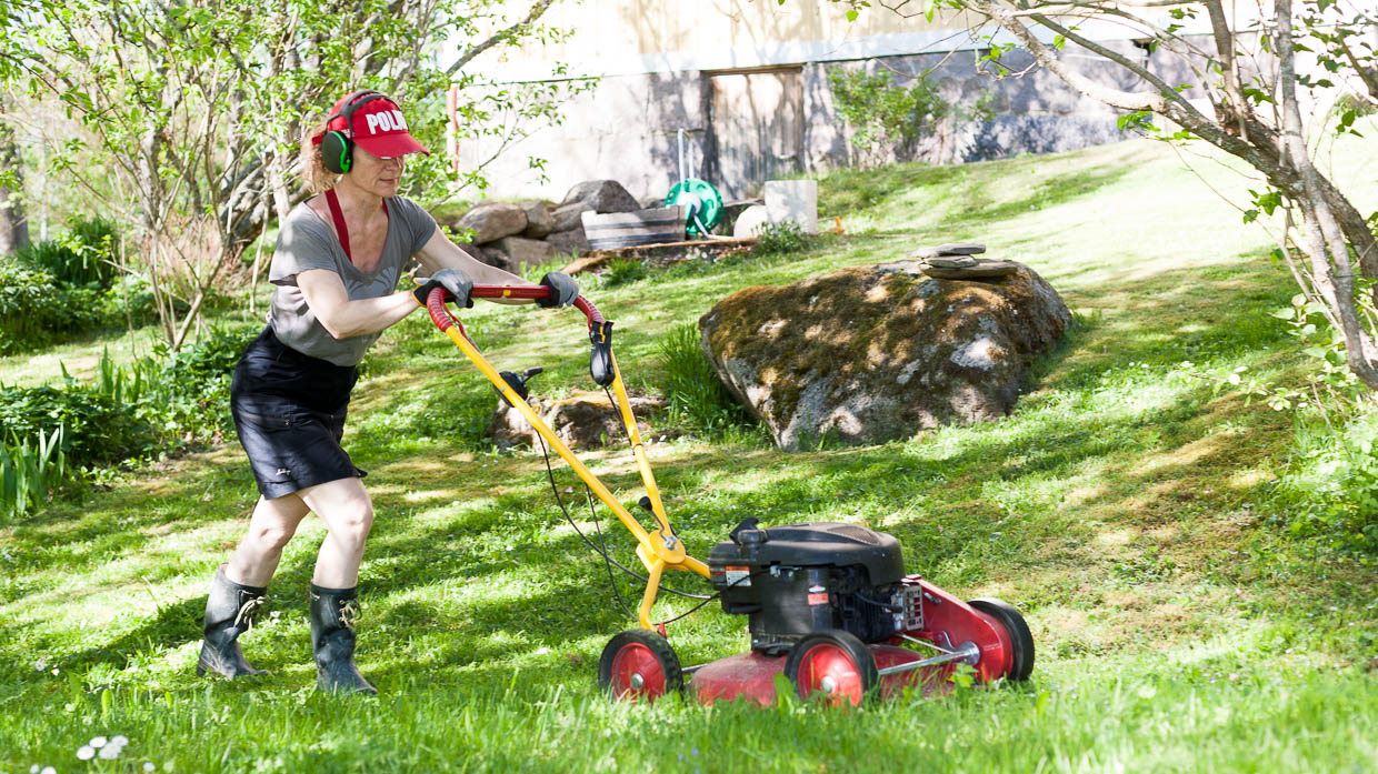 En kvinna klipper gräset en sommardag