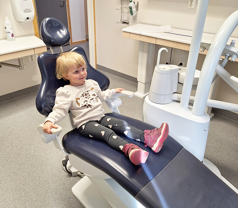 Liten flicka sitter i tandläkarstol och ser glad ut.